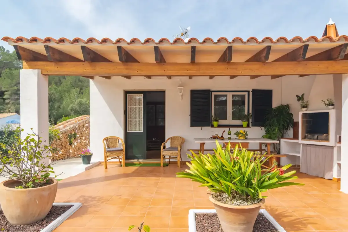 A tiled patio with seating and potted plants sits beneath a wooden roof.