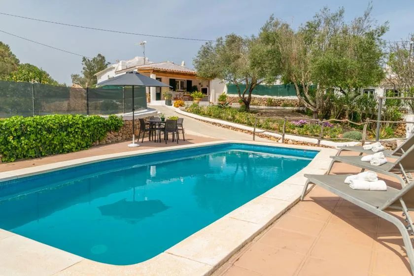 An outdoor swimming pool beside a patio with lounge seating and trees.