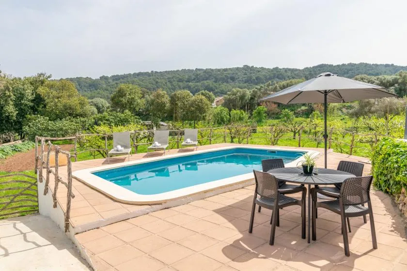 An outdoor swimming pool sits beside a tiled patio with seating and an umbrella.