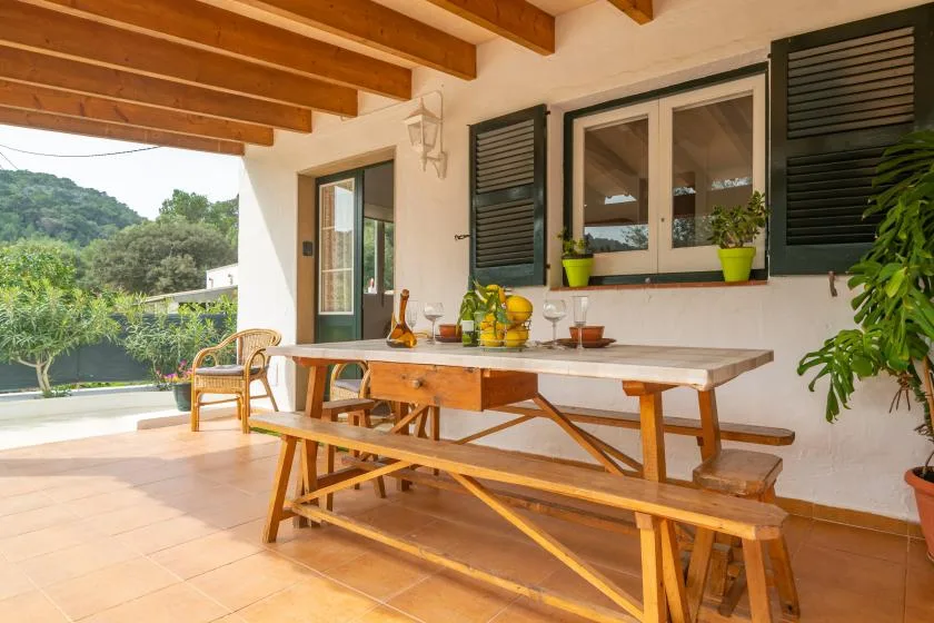 A covered outdoor dining area with a wooden table and chairs beside the garden.