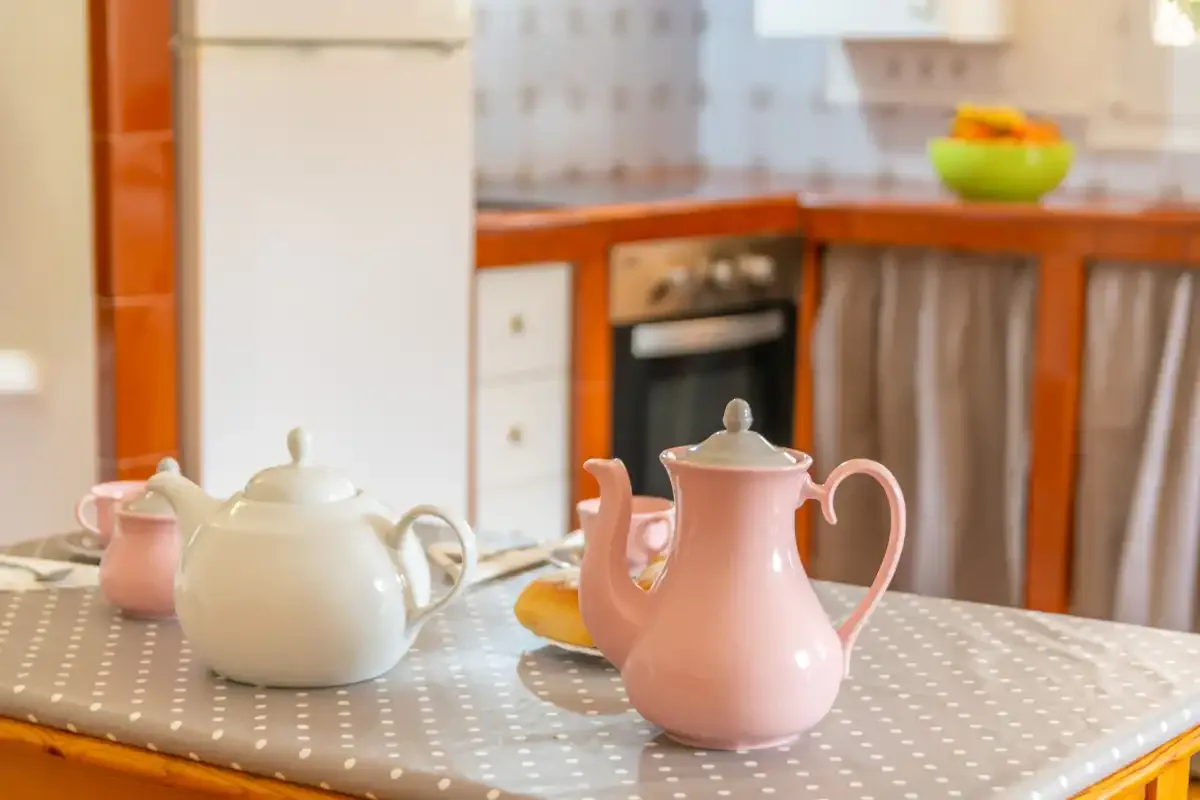 A kitchen table displays a pink teapot and white tea set.