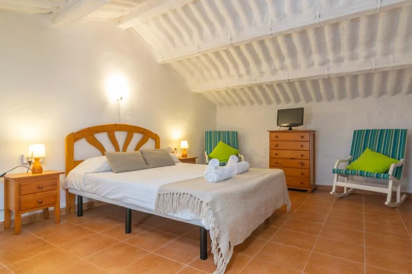 A bedroom with a bed, wooden dressers, and a small seating area.