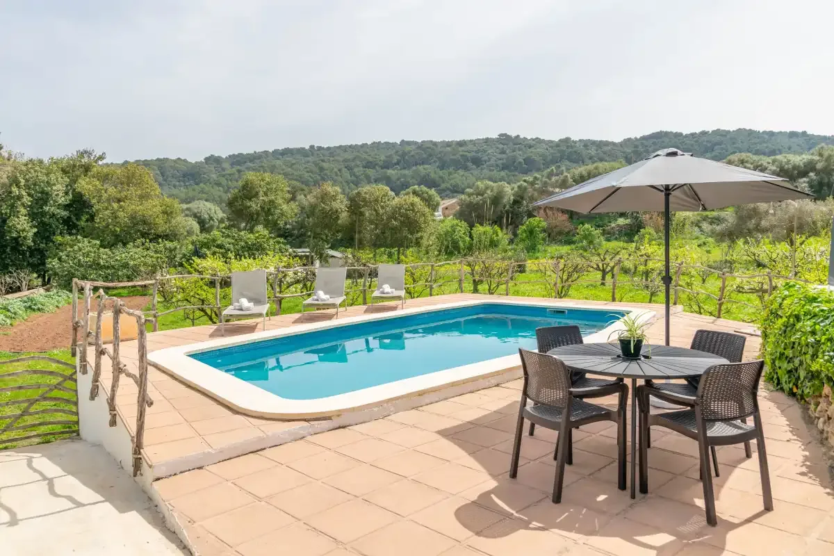 Outdoor swimming pool beside a patio dining area with an umbrella and garden views.