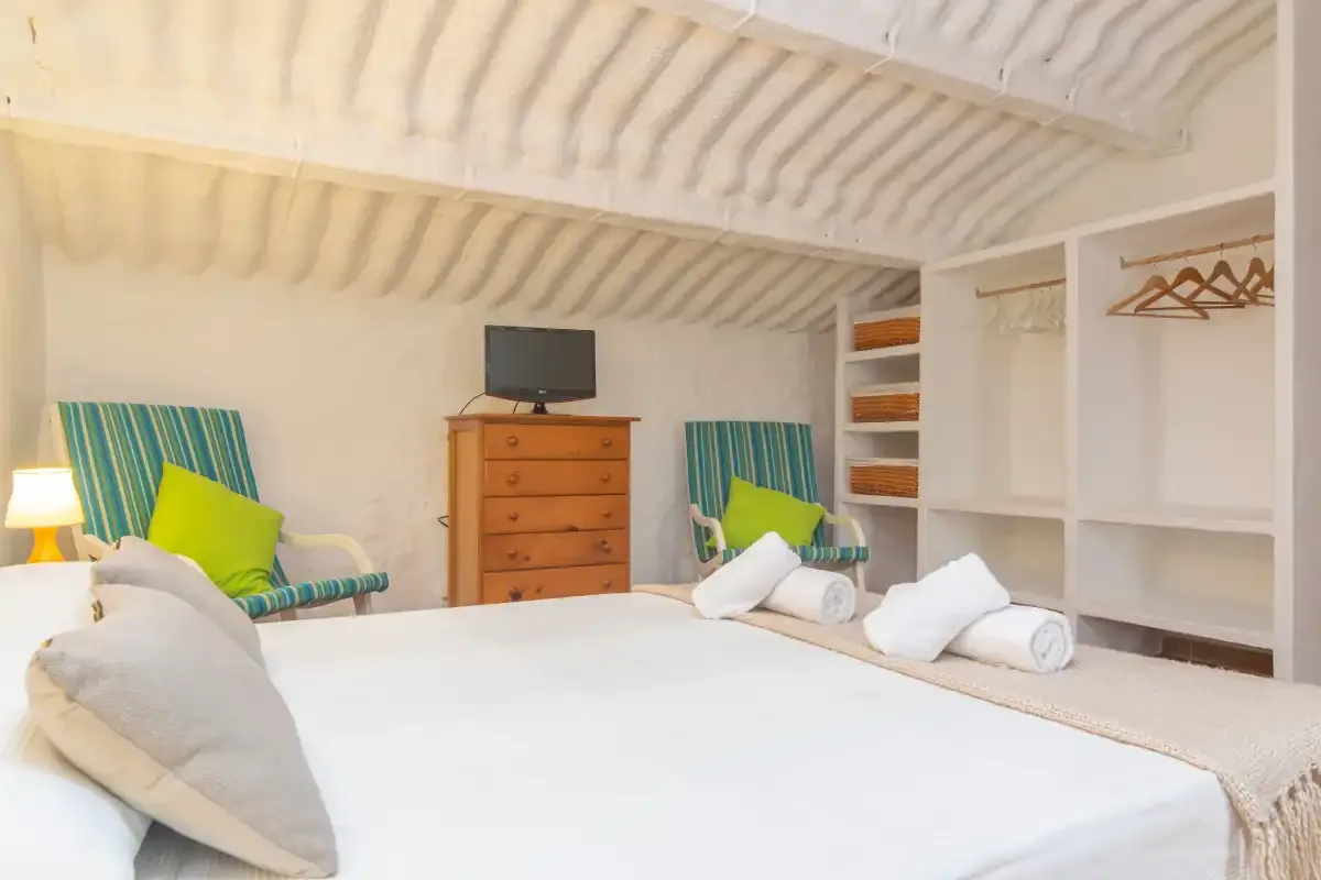 A bright bedroom with a neatly made bed and open shelving.