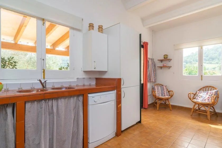 A compact kitchen opens into a sitting area with wicker seating and a window.