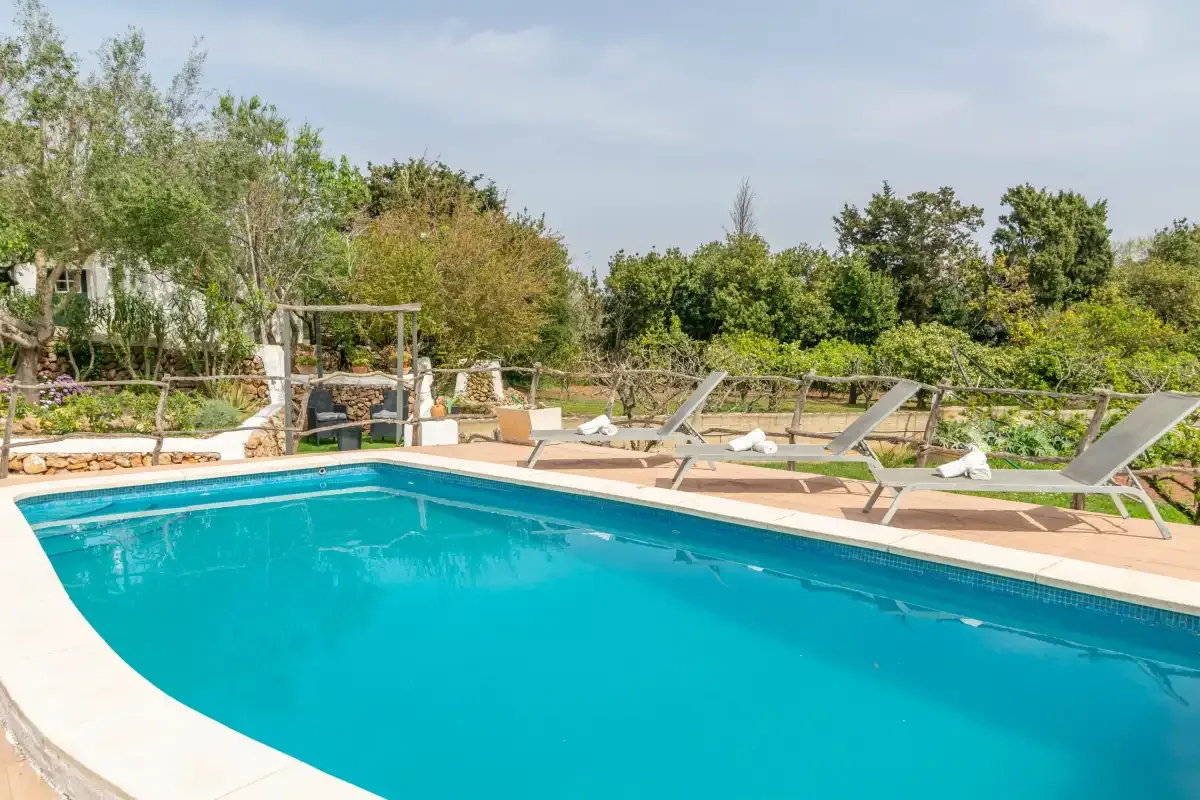 An outdoor swimming pool with lounge chairs and greenery around the deck.