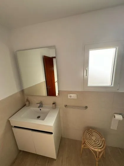 A bathroom with a sink, wall mirror, and a small woven stool.