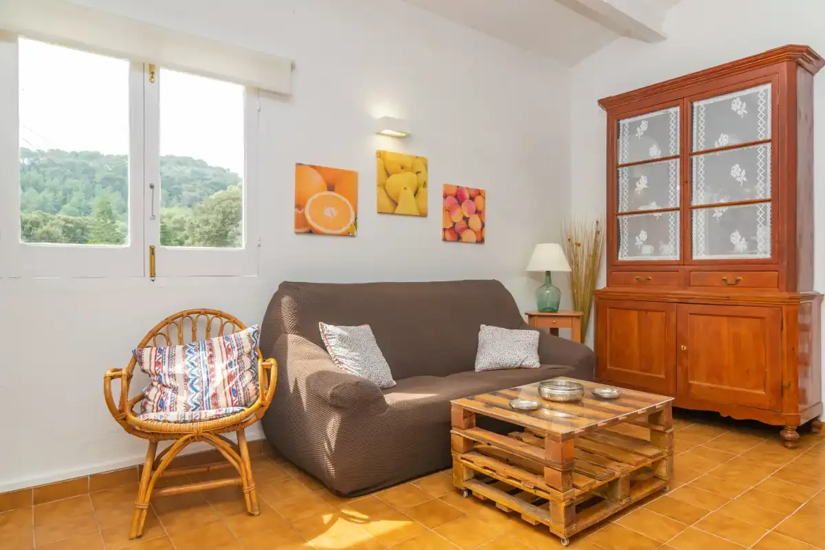 A bright living room has a sofa, a wicker chair, and a wooden cabinet.