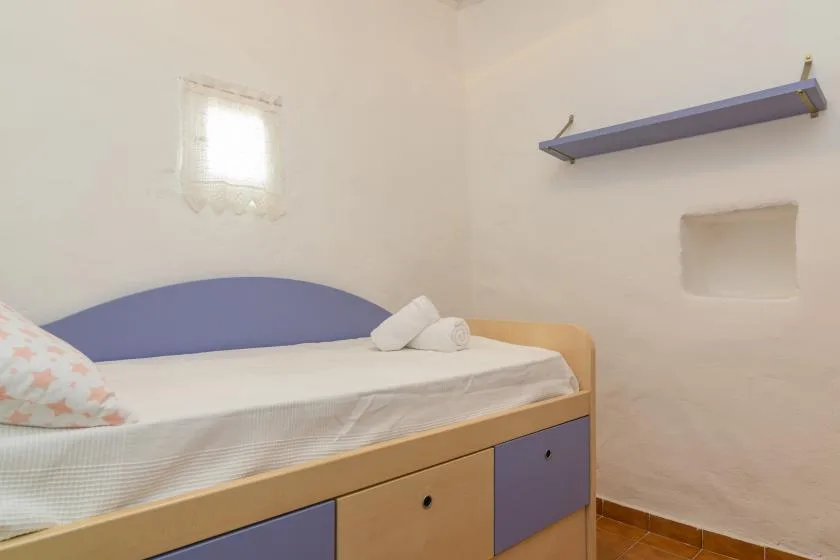 A bedroom with a single bed, a small window, and a wall shelf.