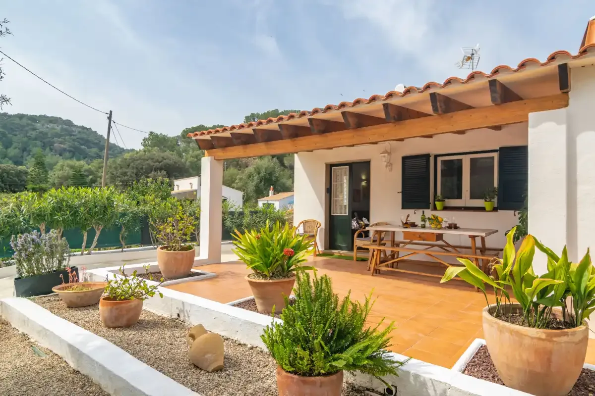 A sunny patio with outdoor seating, potted plants, and a wooden pergola.