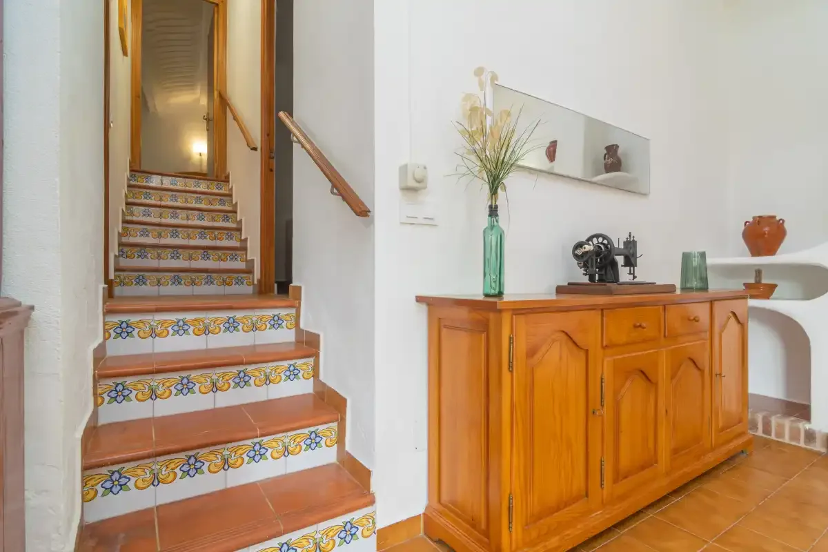 An interior hallway with a tiled staircase and a wooden sideboard.