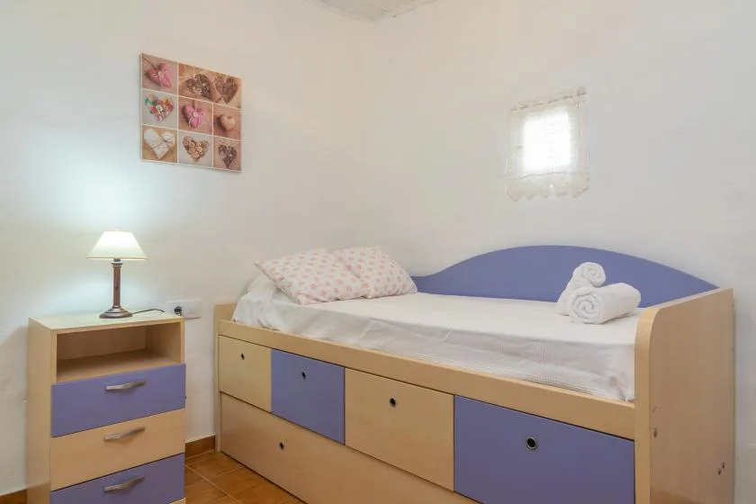 A bedroom with a single bed, patterned pillows, and a bedside table.
