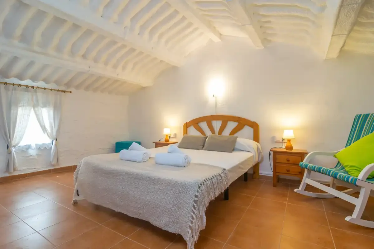 A bedroom with a double bed, bedside tables, and a striped lounge chair.
