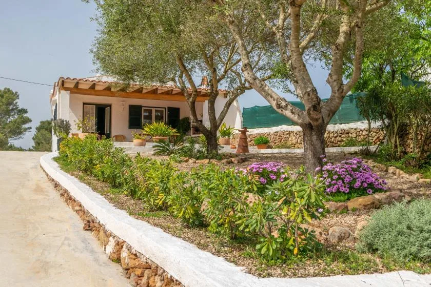 A low house sits beside a landscaped garden with flowering plants and mature trees.
