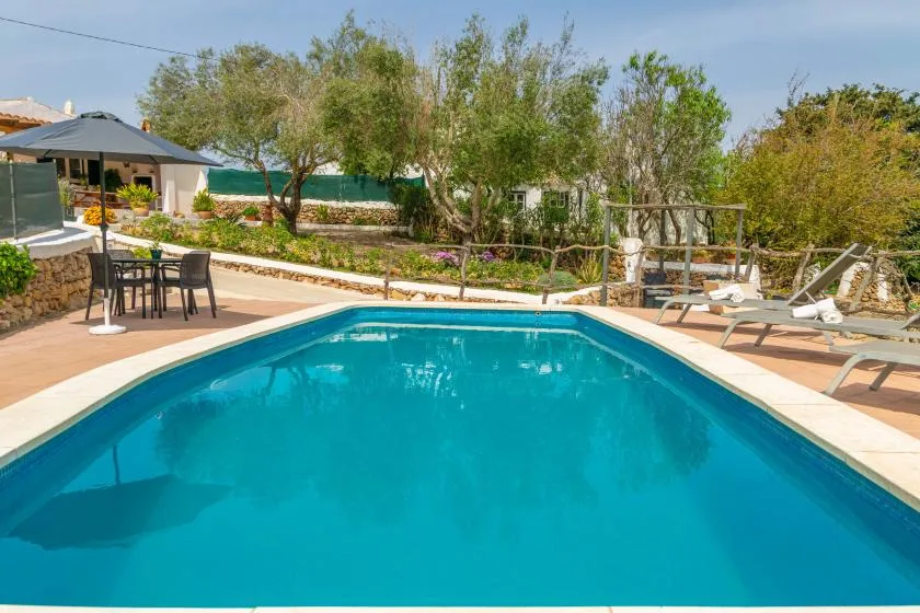 An outdoor swimming pool is surrounded by a paved deck, seating, and trees.