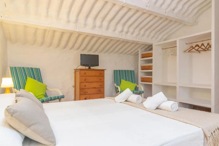 A bedroom with a large bed, striped seating, and a wooden dresser.