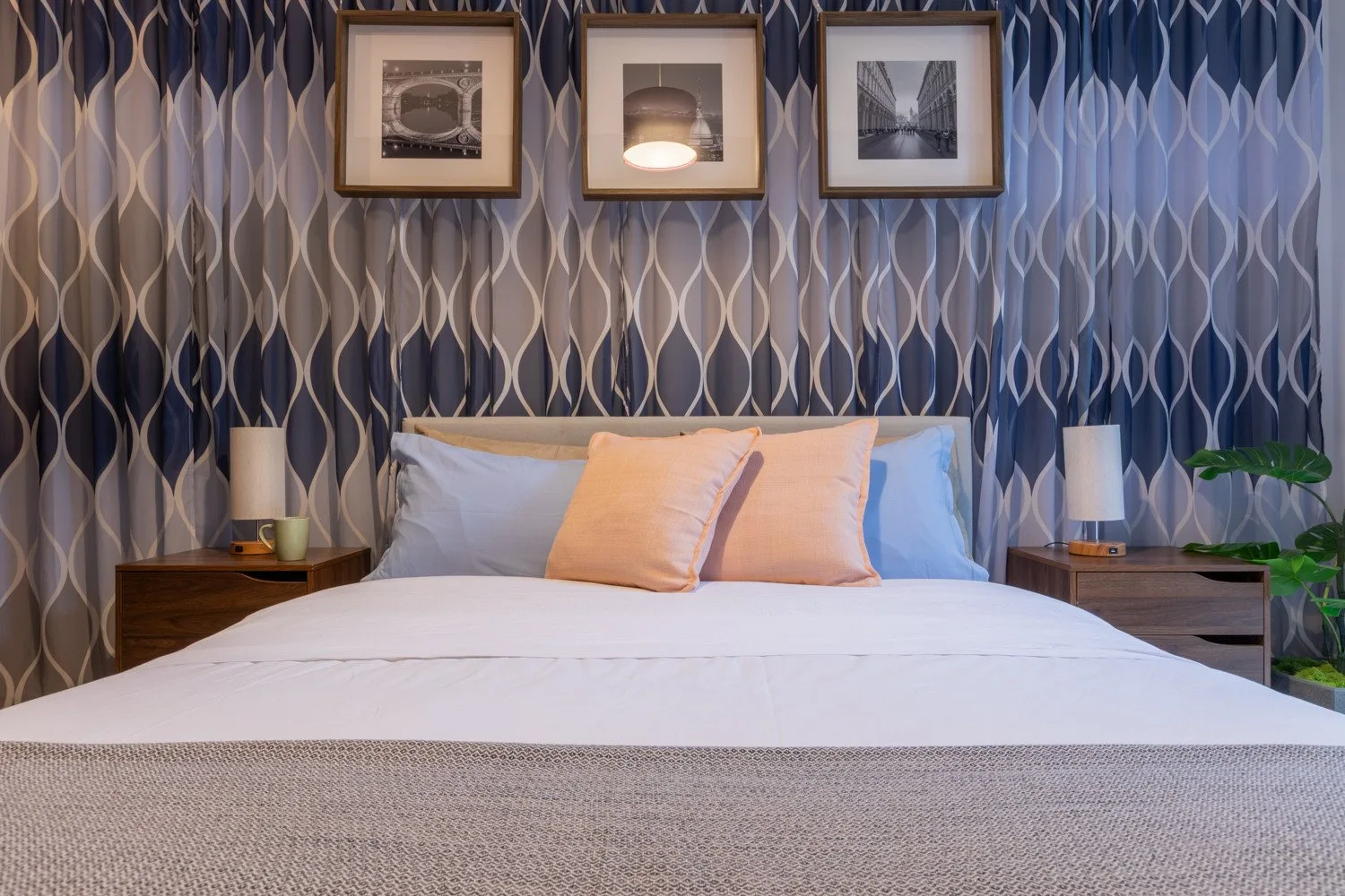 A bedroom with a neatly made bed and patterned wallpaper behind it.