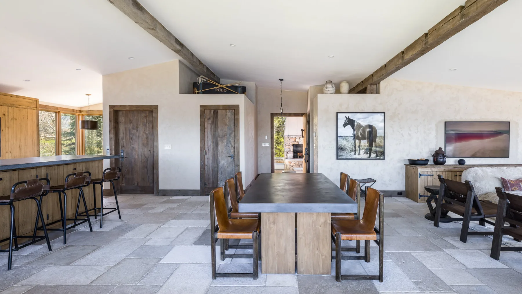 Un amplio comedor con una mesa larga, asientos de barra y grandes ventanas.