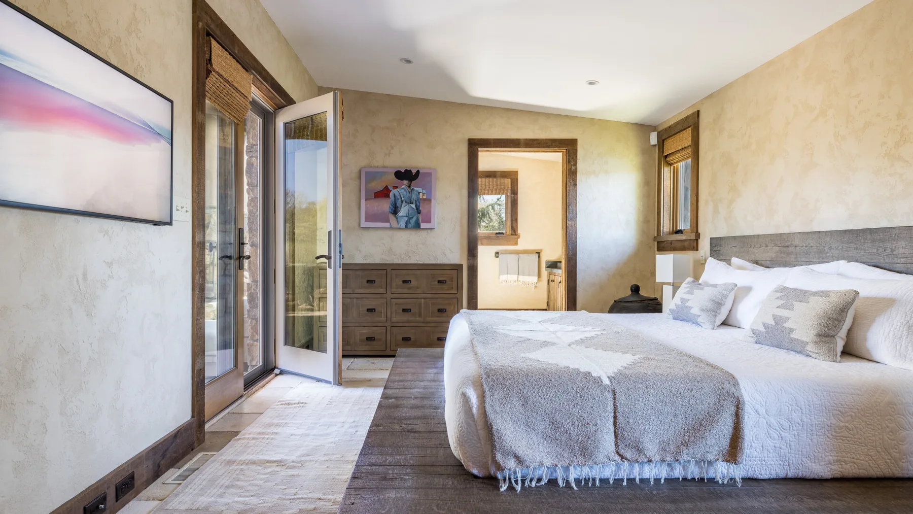 Un dormitorio con una cama, ventanas junto a la cama y una cómoda.