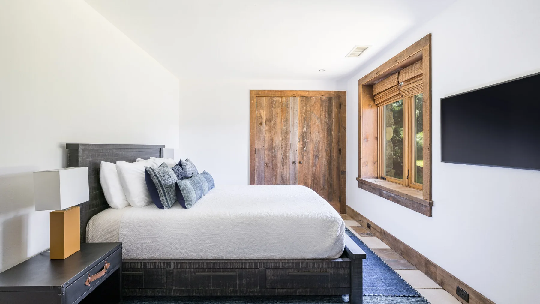 Un dormitorio luminoso con una cama bien hecha, puertas de madera y una ventana.