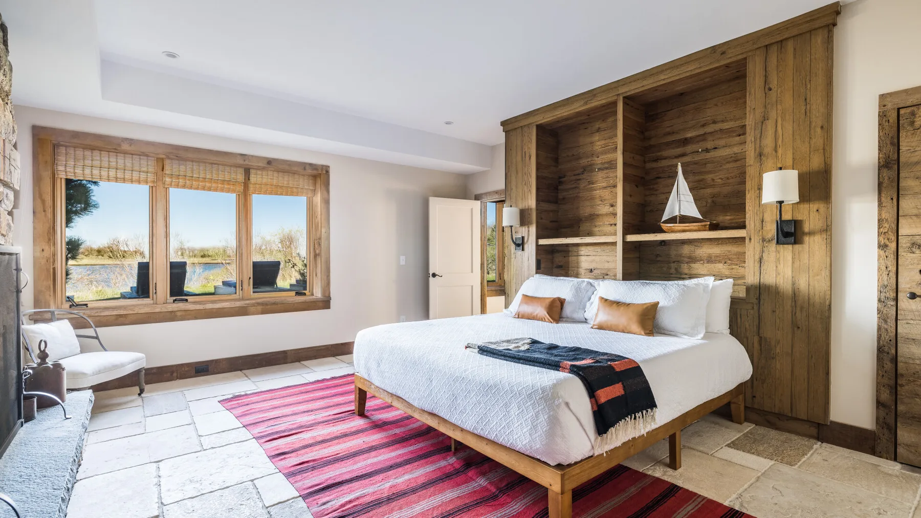 Un dormitorio con una cama junto a una pared revestida de madera y ventanas cerca.
