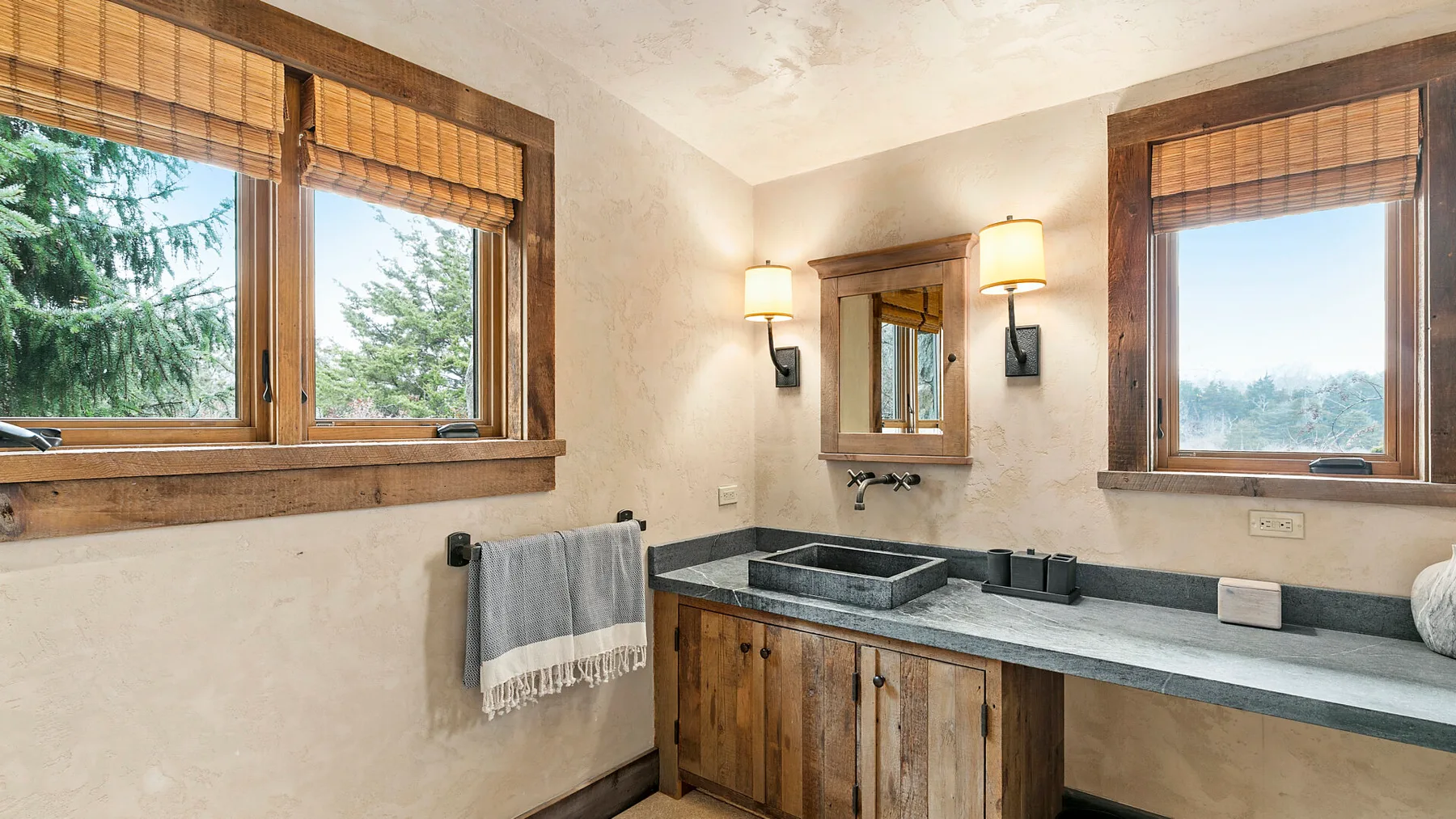 Un lavabo de baño se encuentra entre ventanas con persianas de madera.