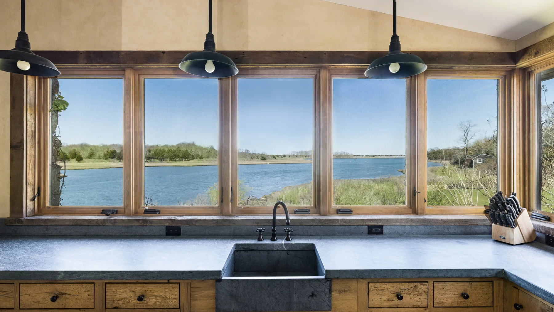 Una encimera de cocina y un fregadero están bajo grandes ventanas con vistas al agua.