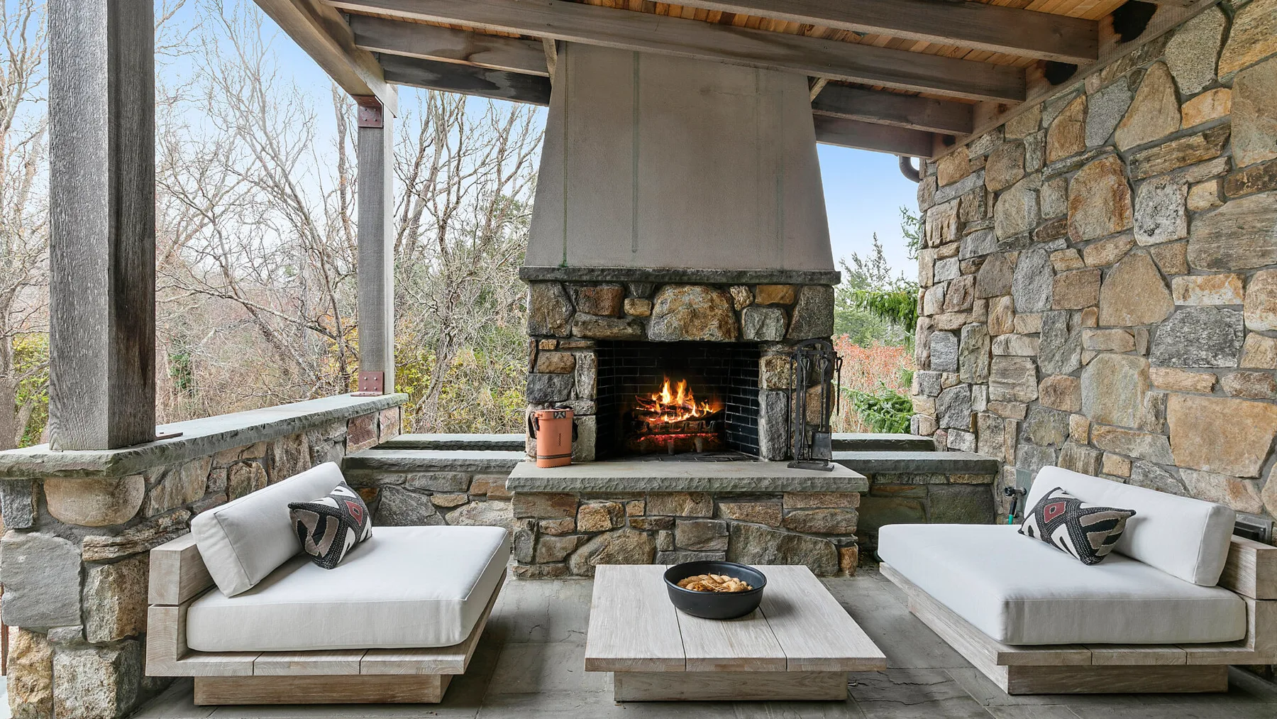 A covered outdoor seating area centers on a stone fireplace and low table.