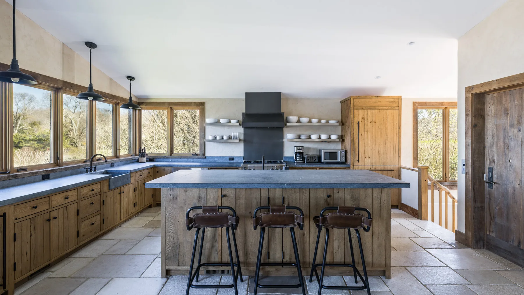 Una cocina amplia con una isla central, gabinetes de madera y grandes ventanas.
