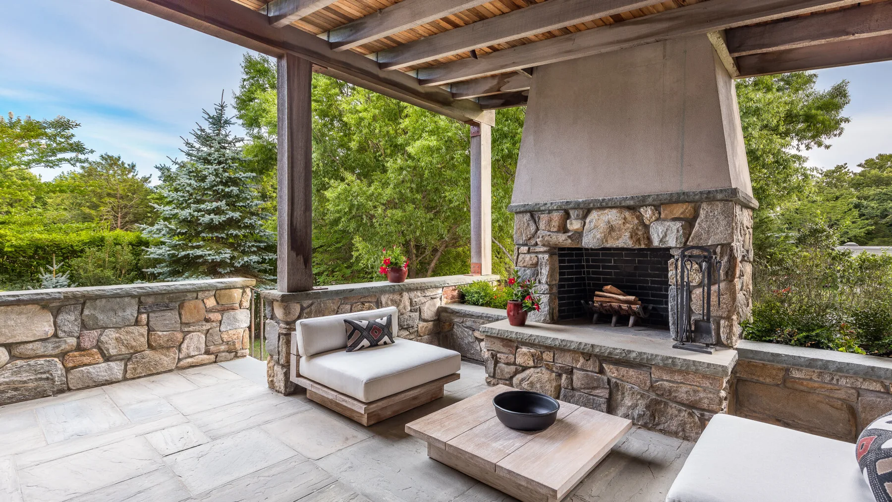 Una zona de estar exterior cubierta con una chimenea de piedra y una mesa baja.