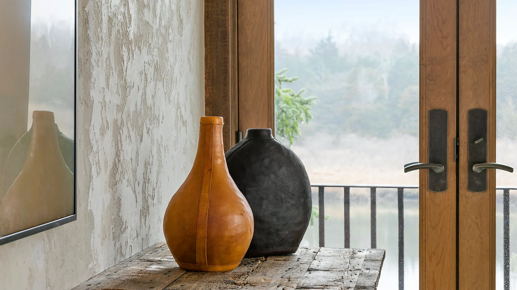 Una mesa de madera con dos jarrones decorativos está junto a una puerta abierta al balcón.
