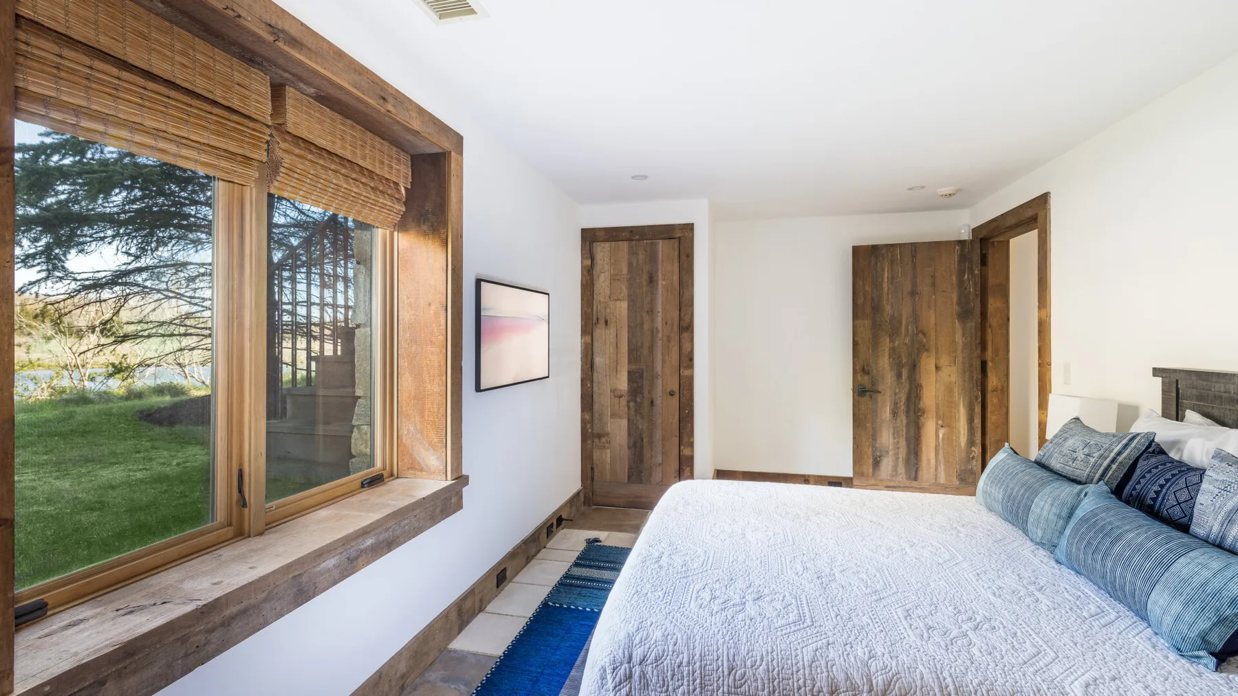 Un dormitorio luminoso con una cama junto a grandes ventanas con vistas a un césped verde.