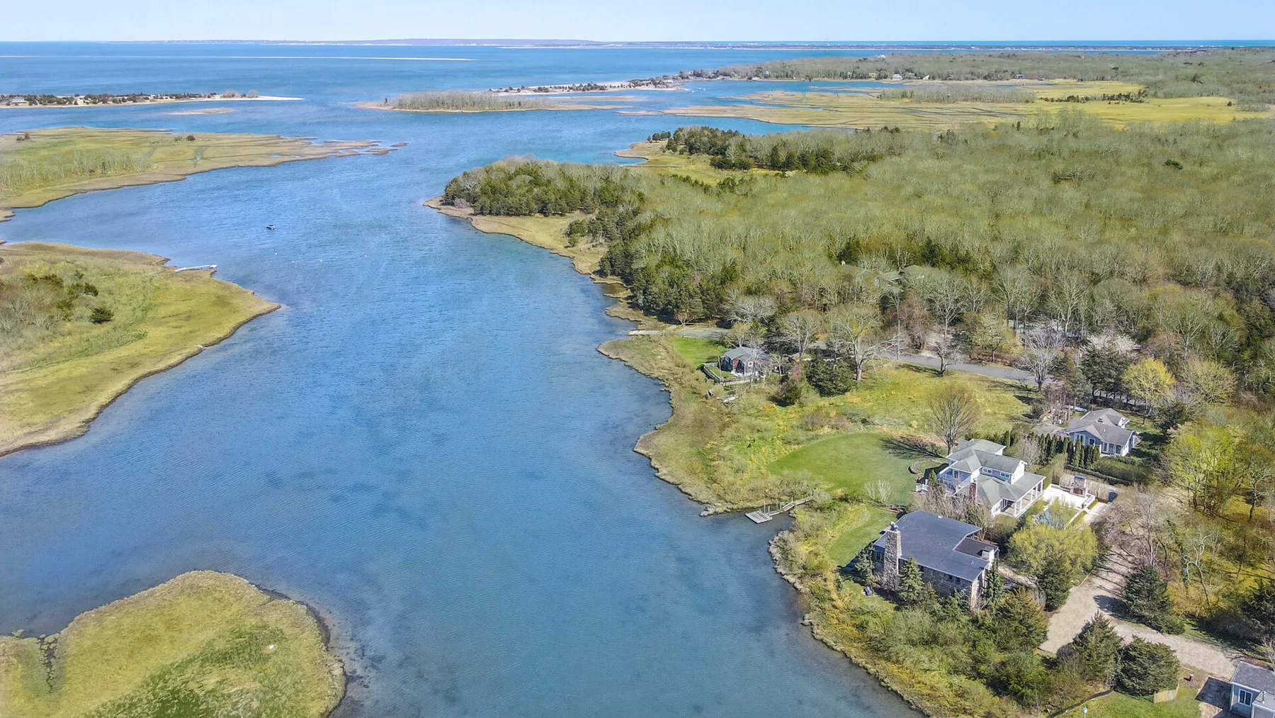 Vista aérea de un canal sinuoso entre marismas verdes, con casas junto a la orilla.