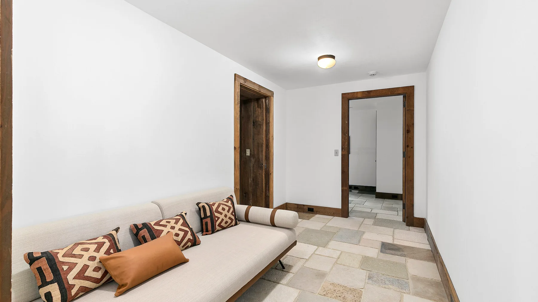 Una habitación estrecha tiene una larga zona de asiento acolchada y dos puertas.