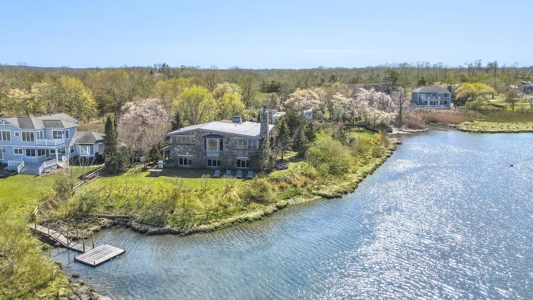 Aerial view of houses along a wooded shoreline beside a lake.