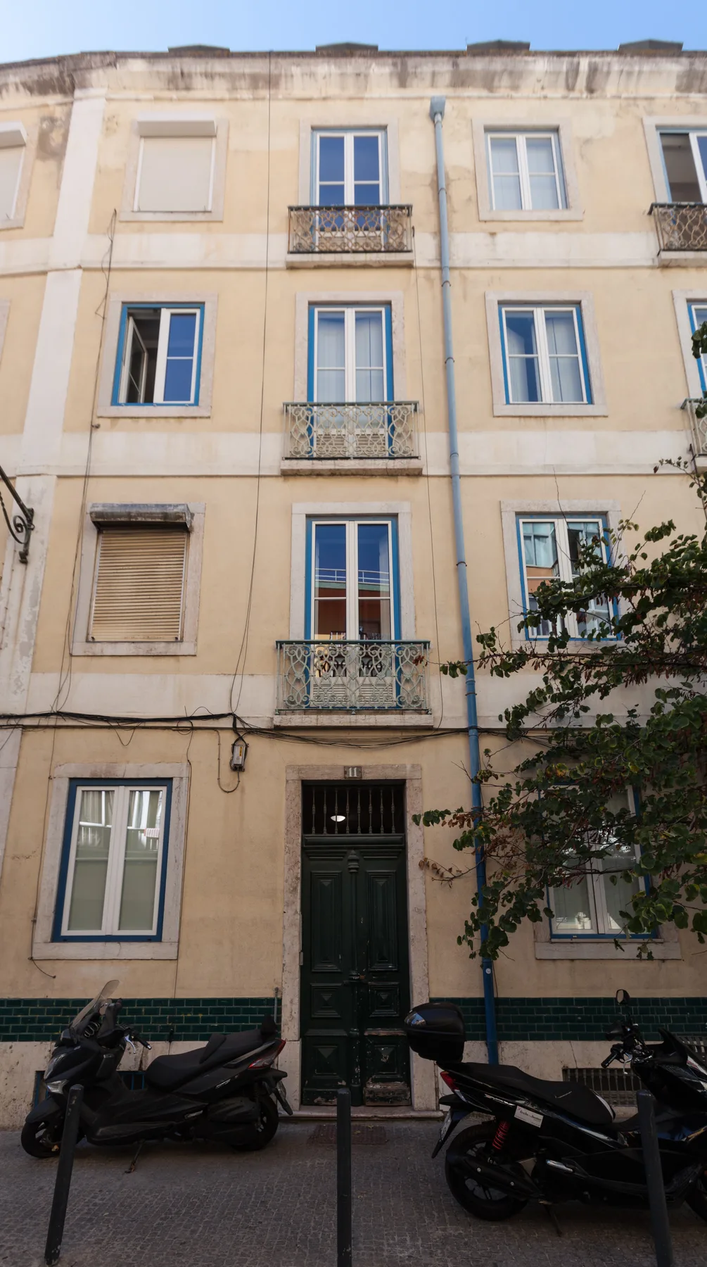Fachada de un edificio de apartamentos claro, con ventanas azules y pequeños balcones.