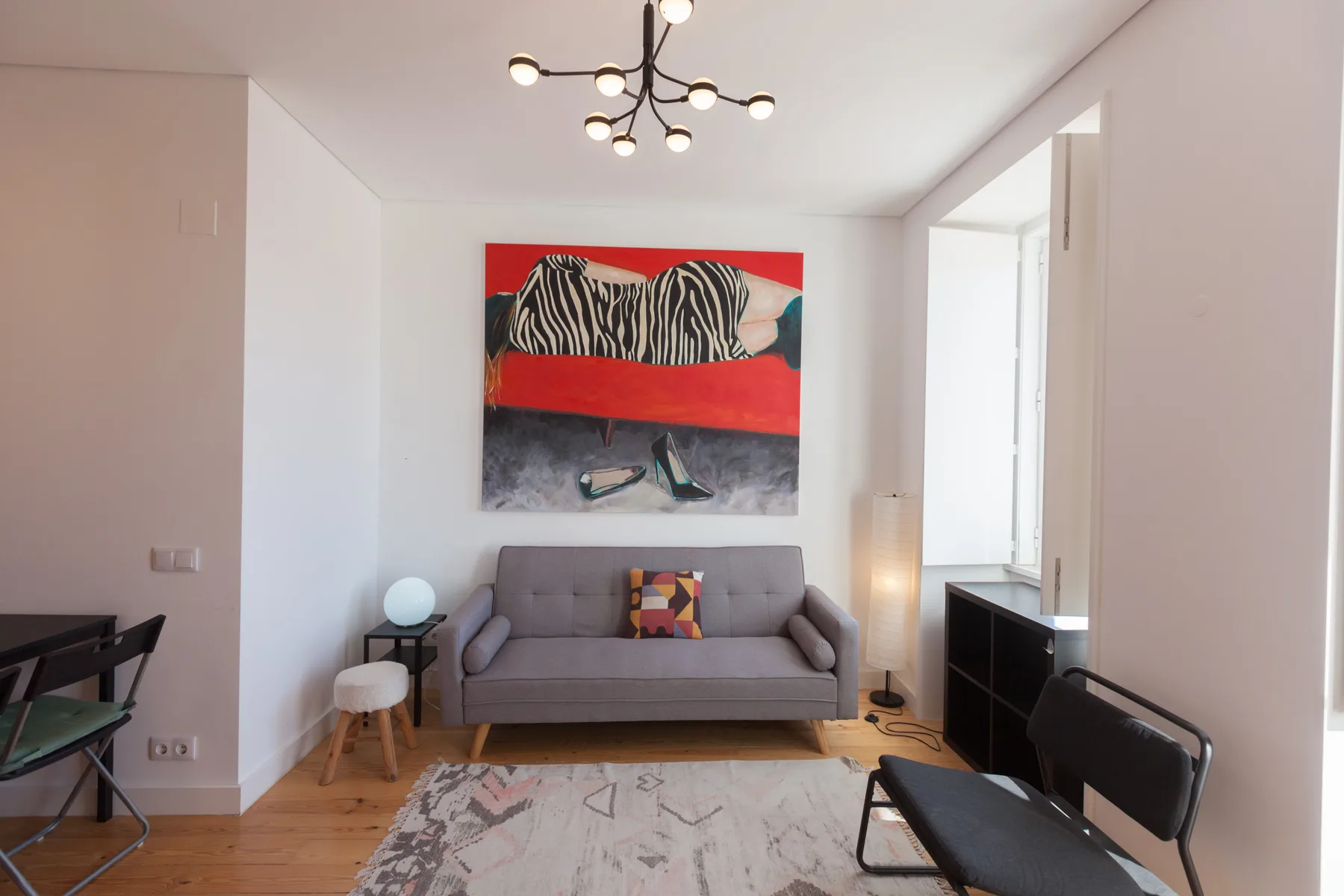 Una sala de estar luminosa con un sofá gris y arte colorido en la pared.