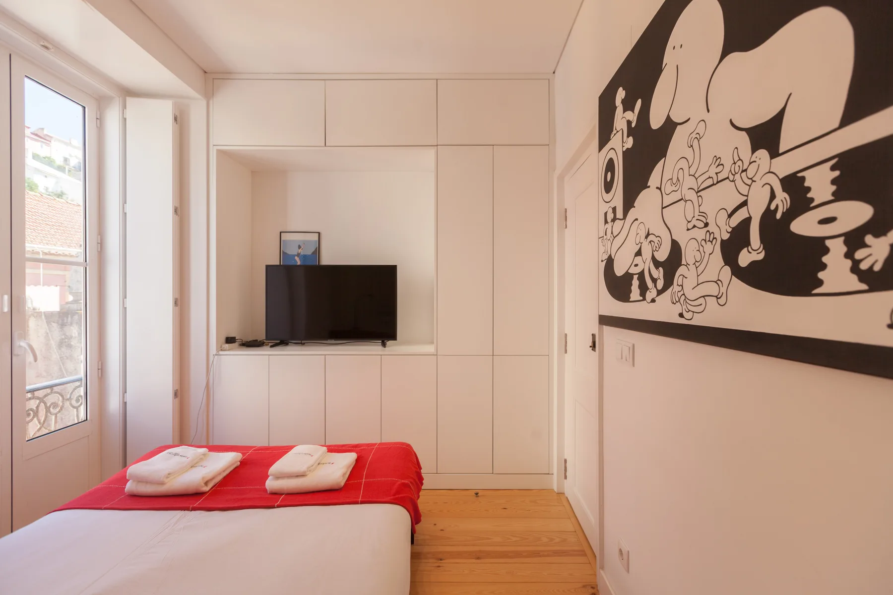 Un dormitorio con cama, televisor y un gran mural en blanco y negro.