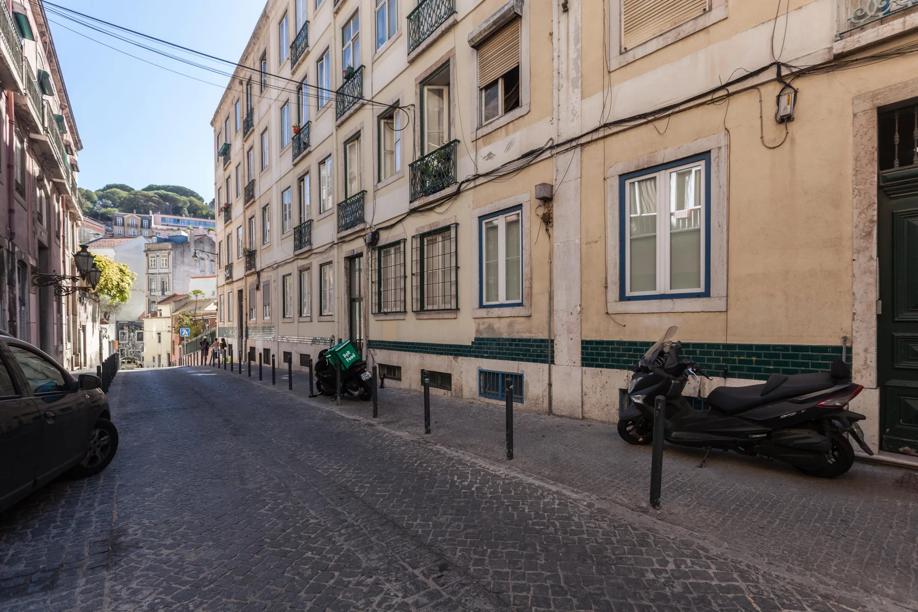 Una calle estrecha adoquinada pasa entre edificios de apartamentos, con scooters estacionados junto a la acera.