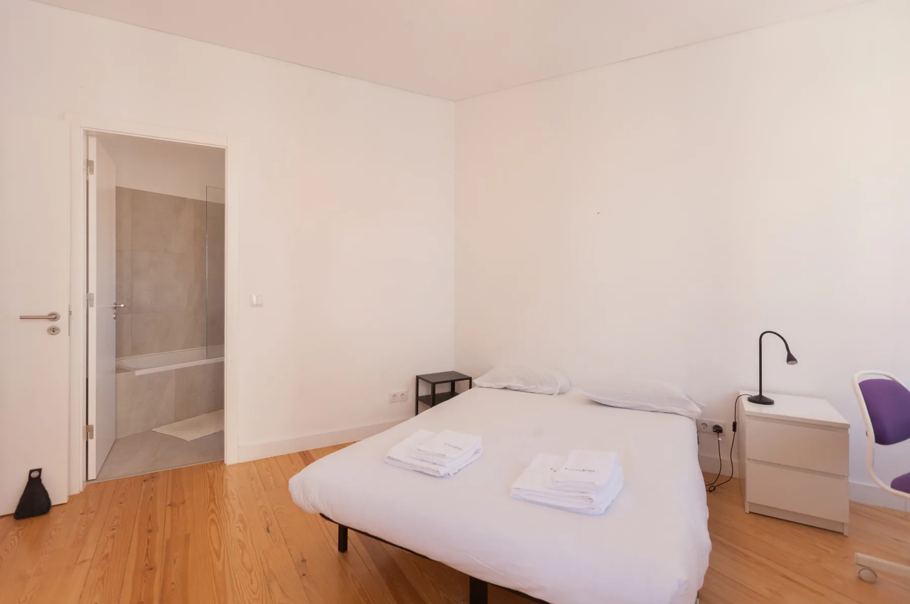 Un dormitorio con una cama, una mesita de noche y una puerta abierta al baño.