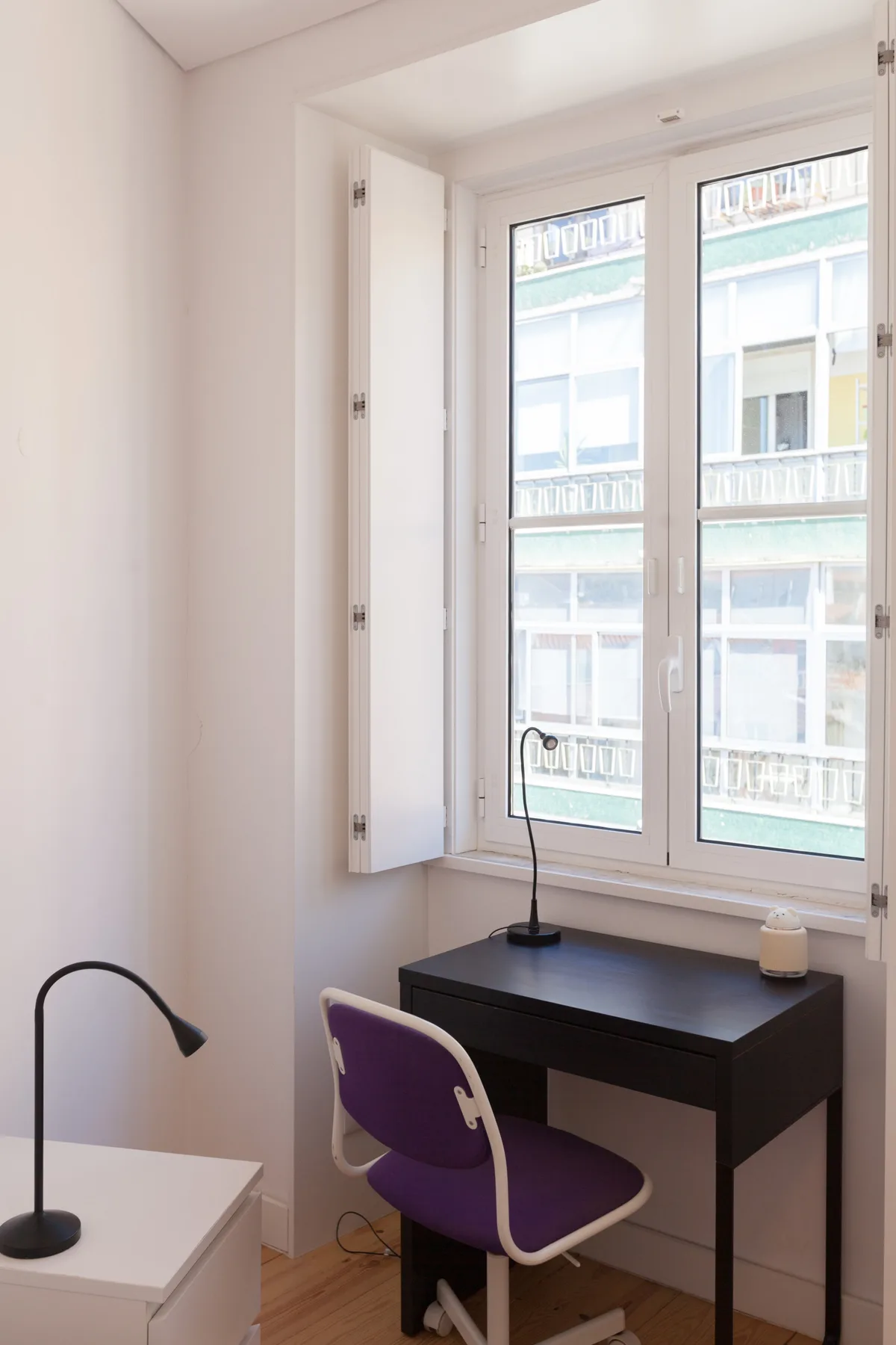 Un escritorio y una silla están junto a ventanas altas en una habitación luminosa.