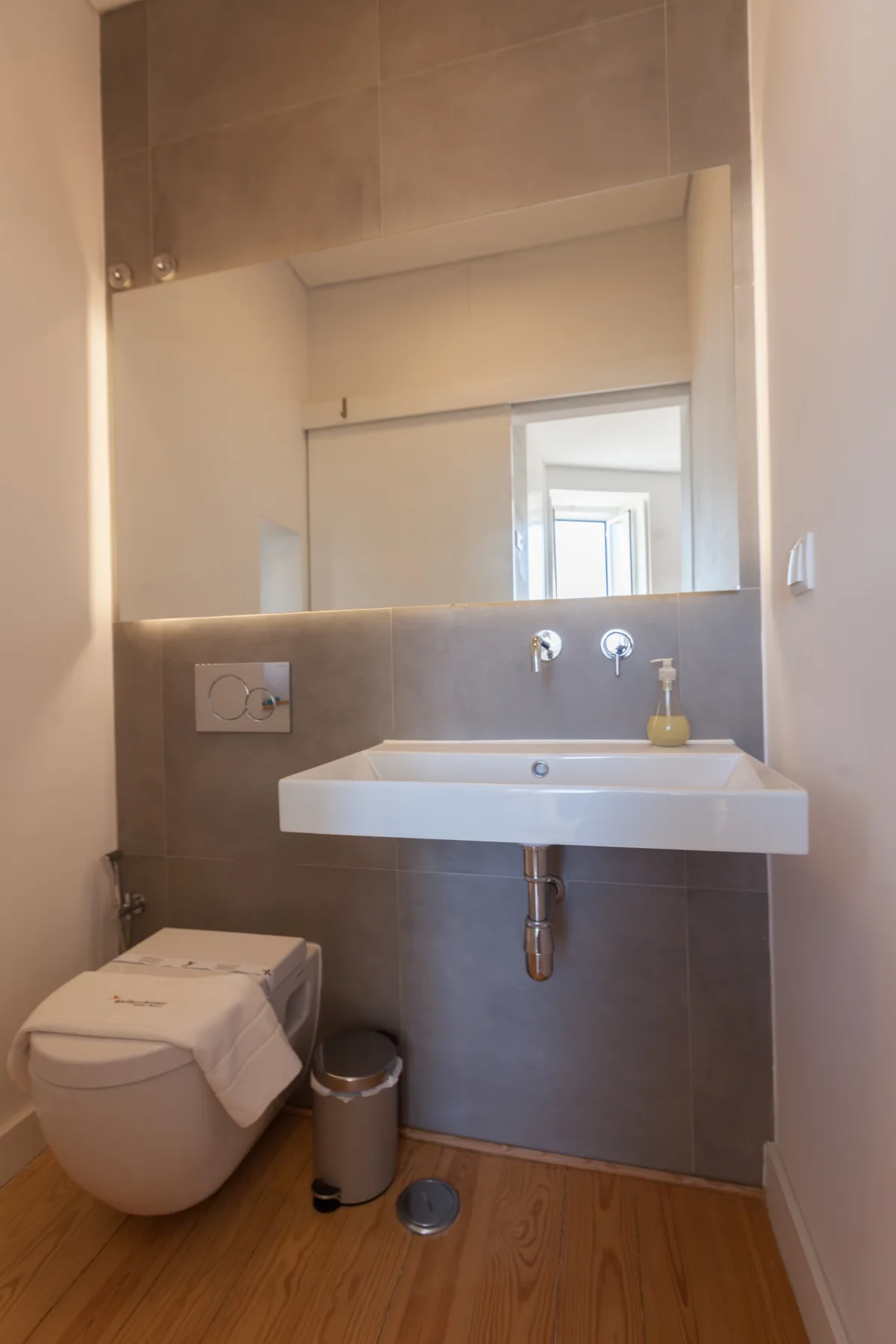 Un baño con lavabo suspendido, espejo e inodoro.