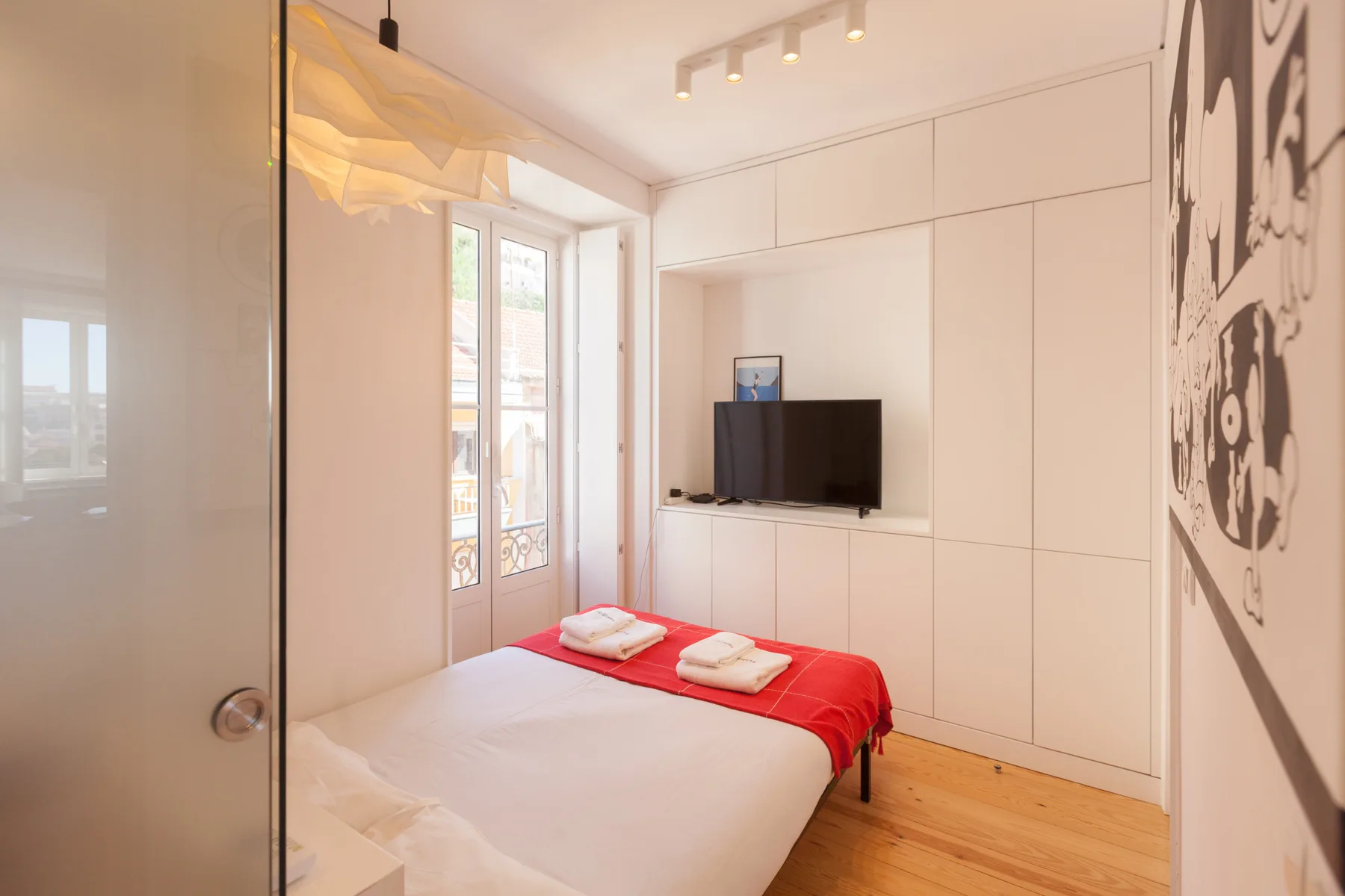 Un dormitorio luminoso con una cama y un televisor montado en la pared.
