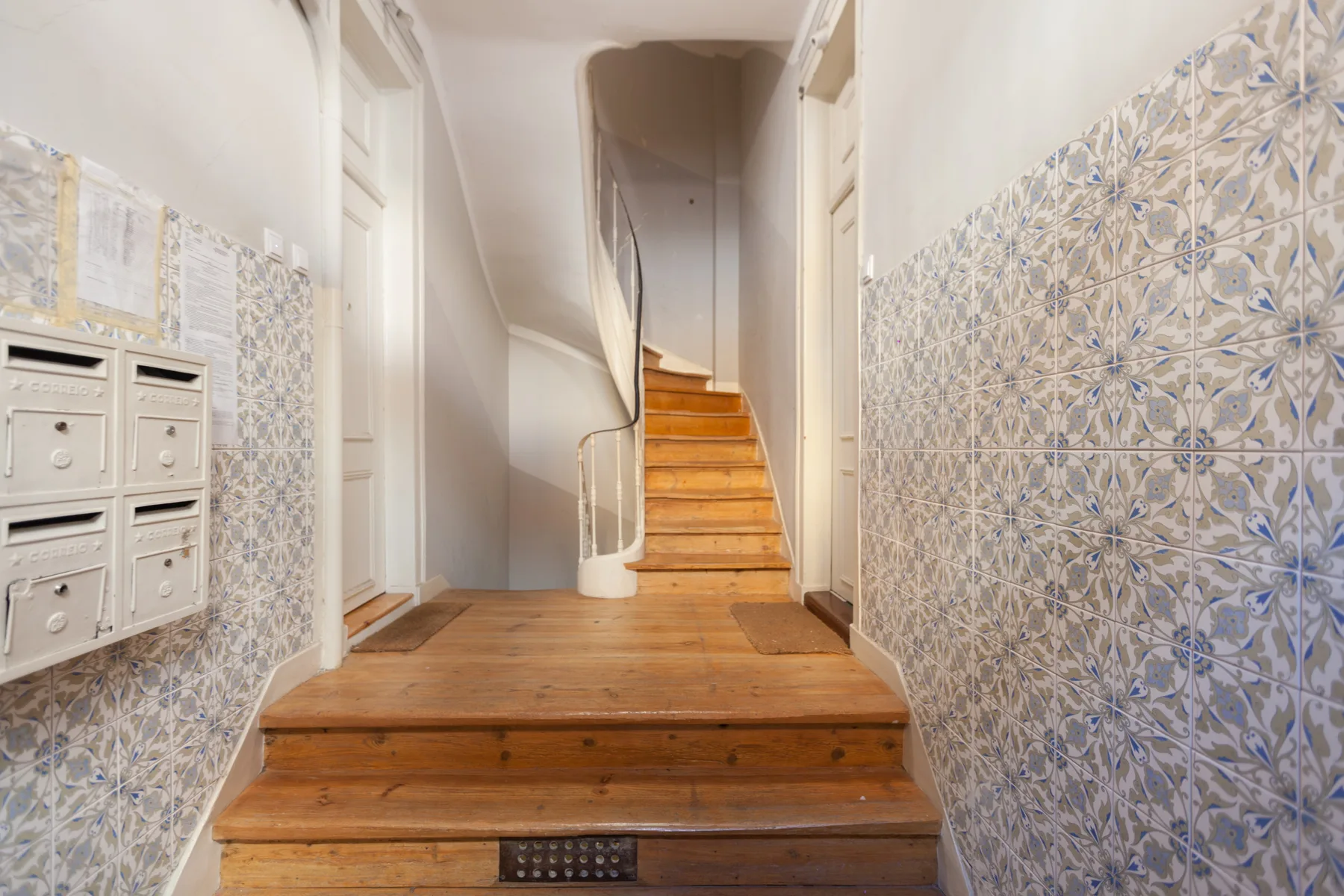 Un pasillo interior con escaleras de madera y paredes de azulejos estampados.