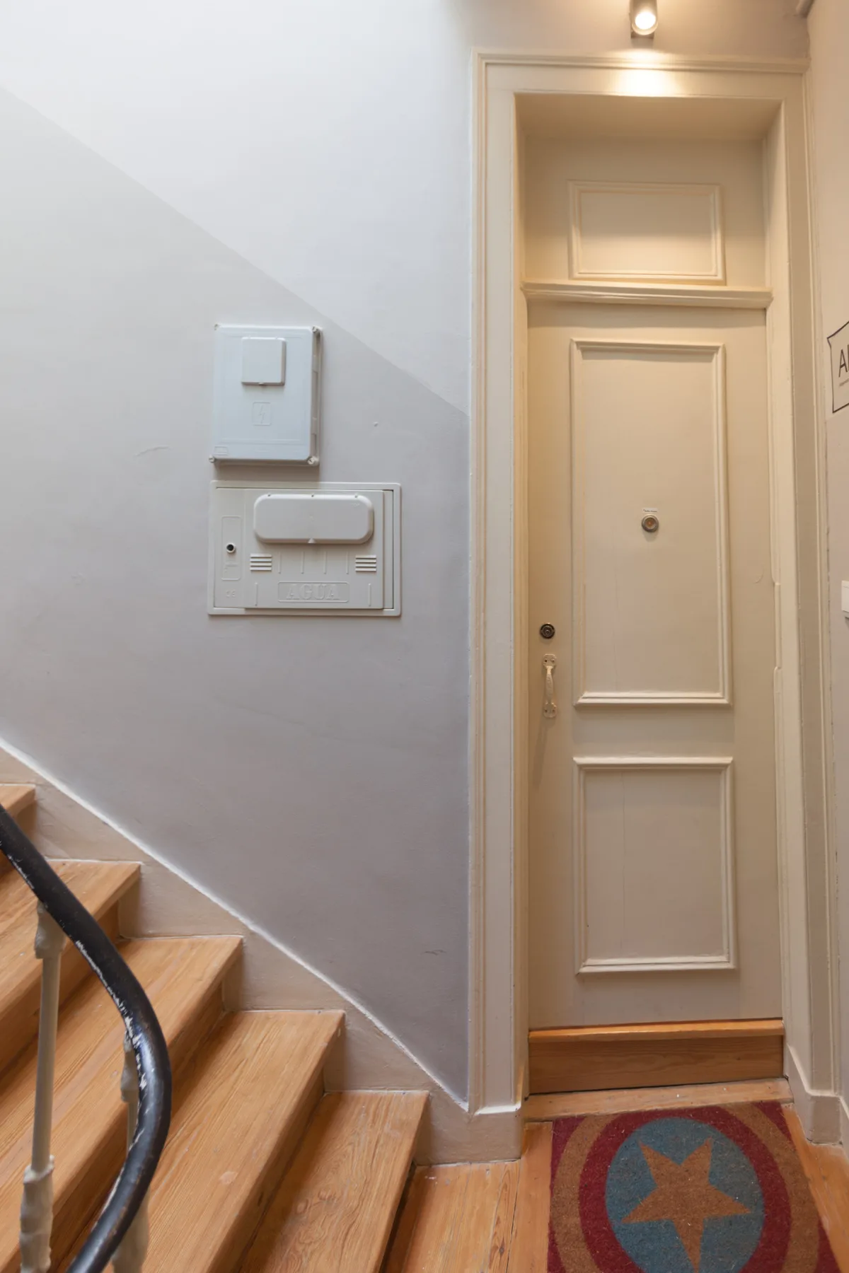 Una entrada interior con una puerta panelada junto a una escalera de madera.