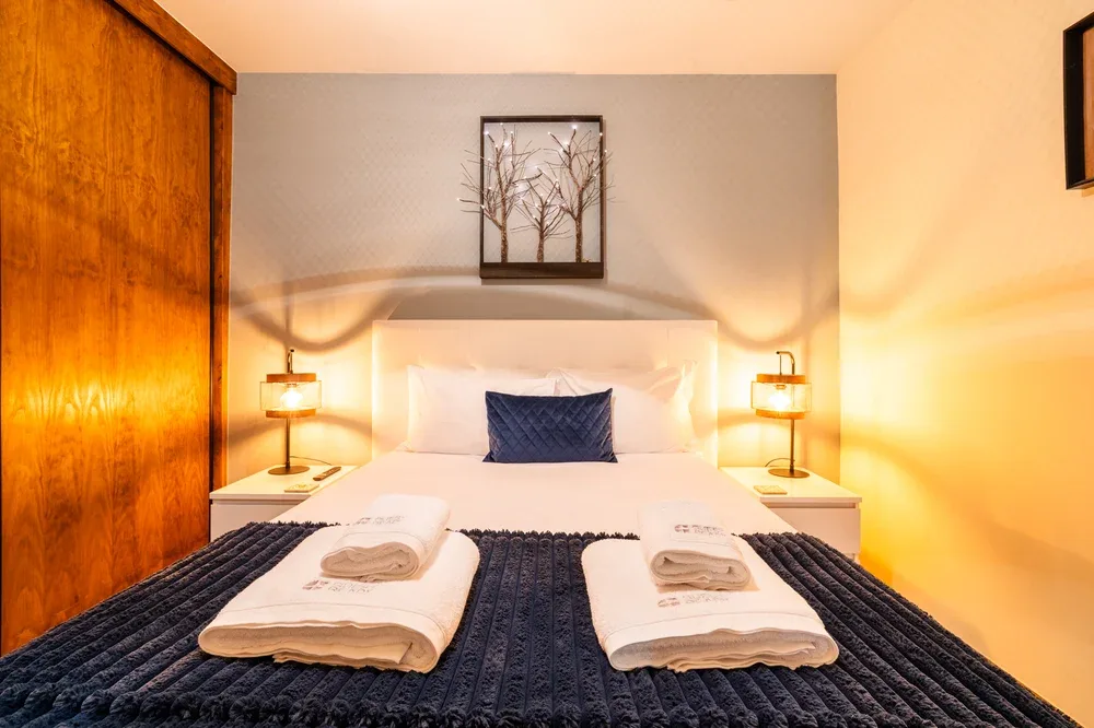 Un dormitorio con una cama bien tendida, toallas dobladas y lámparas a ambos lados.