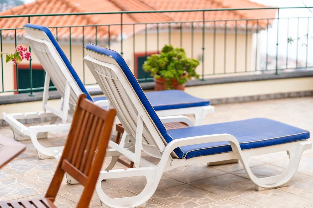 Una terraza soleada con tumbonas de cojines azules y plantas en macetas.