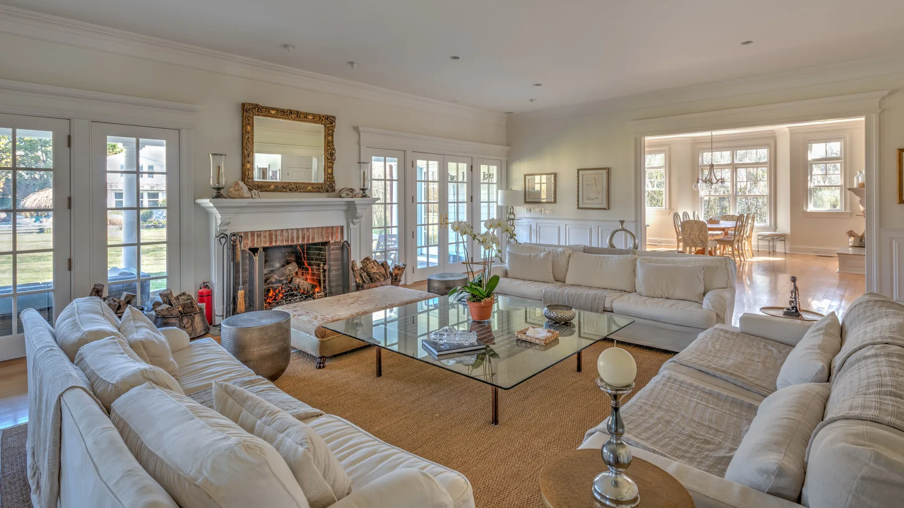 A bright living room with seating arranged around a glass coffee table and fireplace.