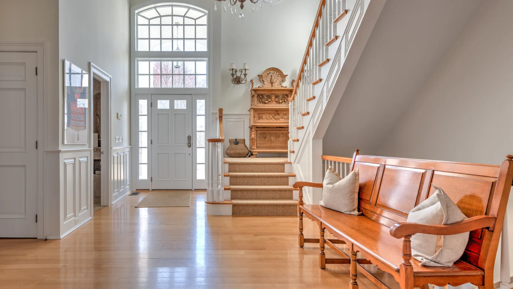 A bright entry hall with a staircase and wooden bench.