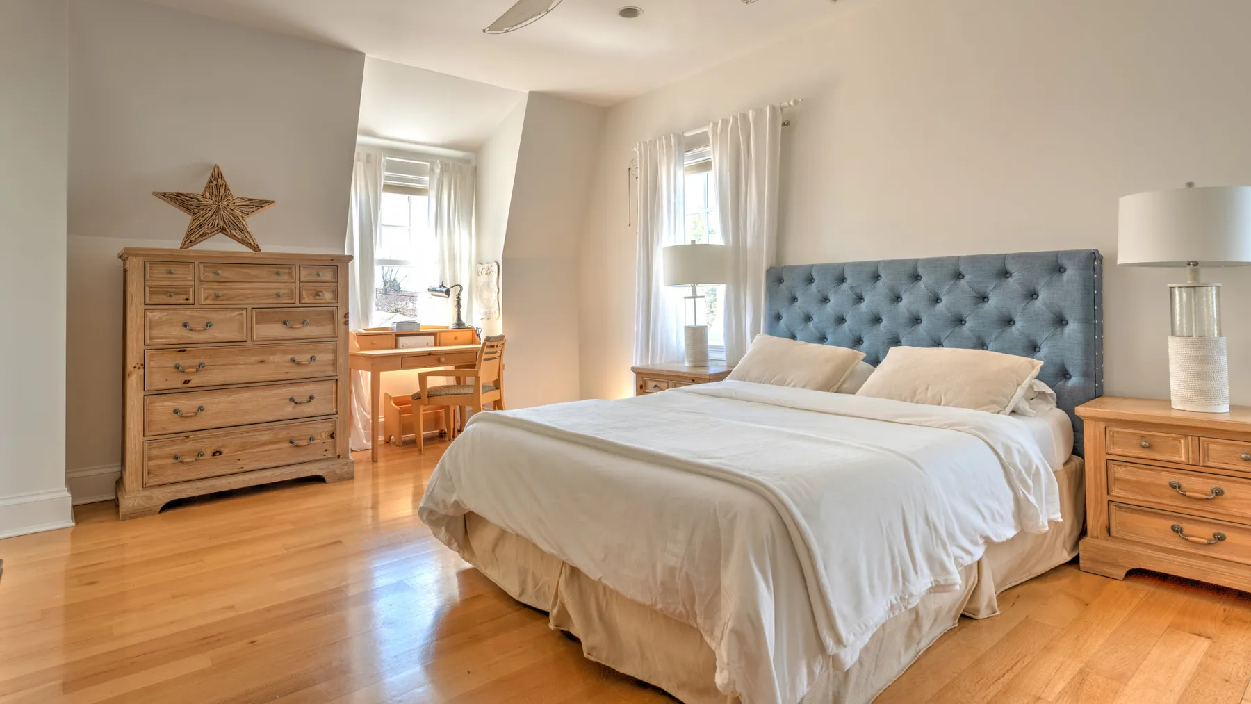 A bright bedroom with a large bed and a small desk by the windows.